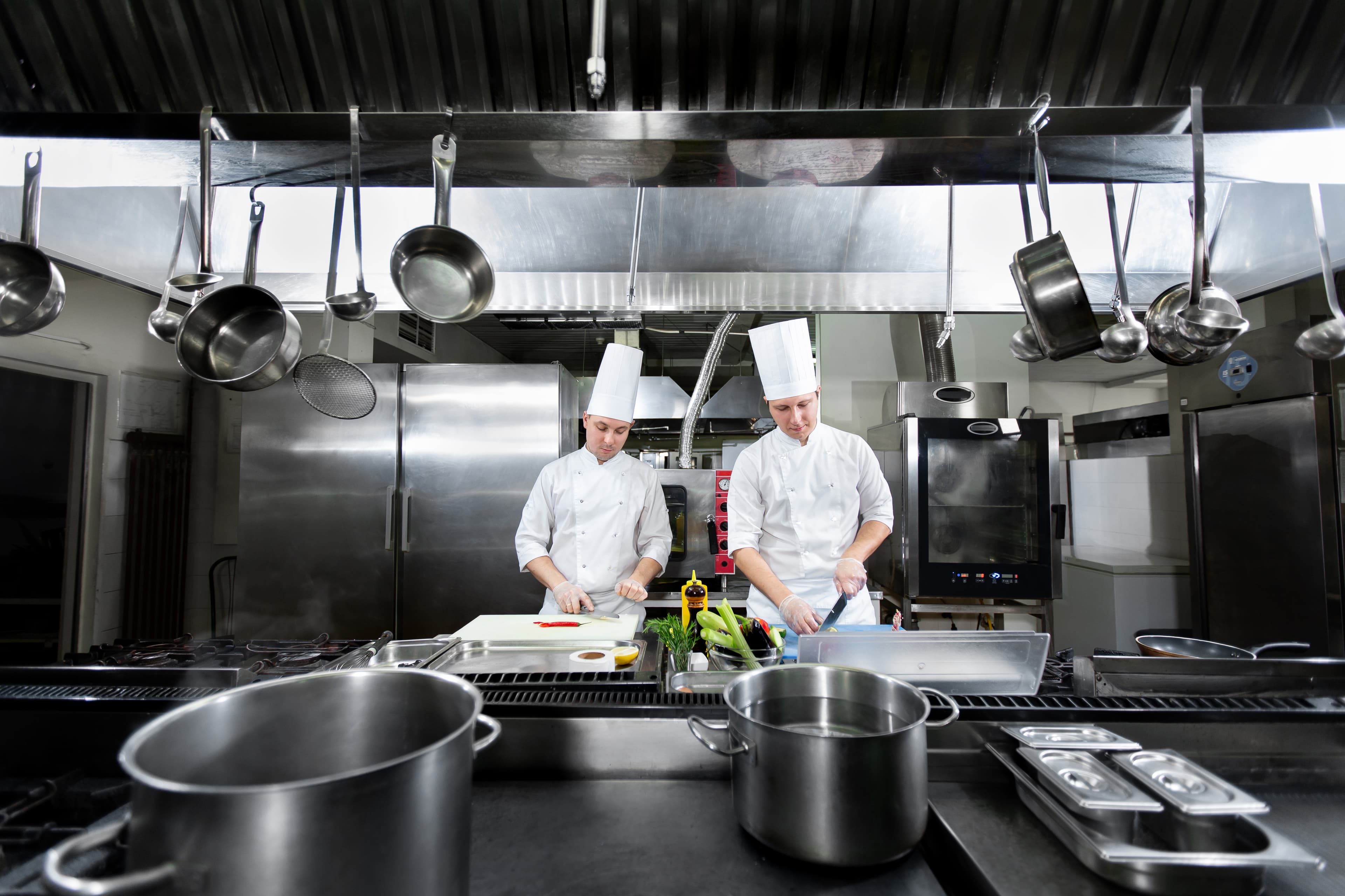 Pristine commercial kitchen — chefs at the prep line, hanging pots